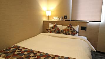 A hotel room with a neatly made bed, a patterned throw blanket, and a bedside lamp.