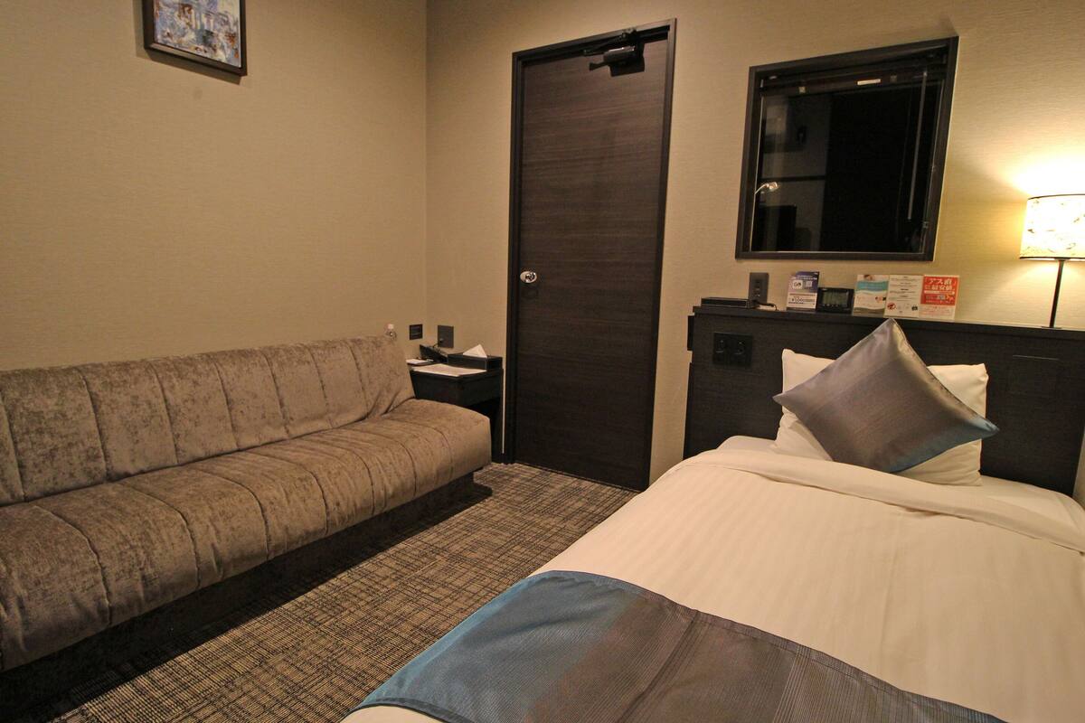 A hotel room with a bed, a sofa, a desk, and a door.