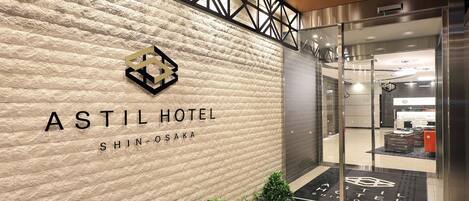 The exterior of the Astil Hotel Shin-Osaka with a textured stone facade, a logo above the name, and a glass entrance leading to the interior.