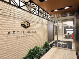 Exterior del Hotel Astil Shin-Osaka, con fachada de piedra texturizada, un logotipo sobre el nombre y una entrada de vidrio hacia el interior.