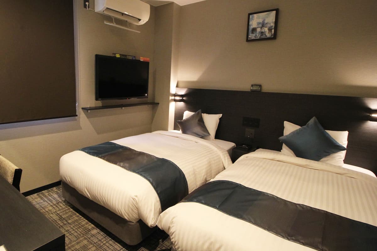 A hotel room with two beds, a flat-screen TV, an air conditioner, and a painting on the wall.