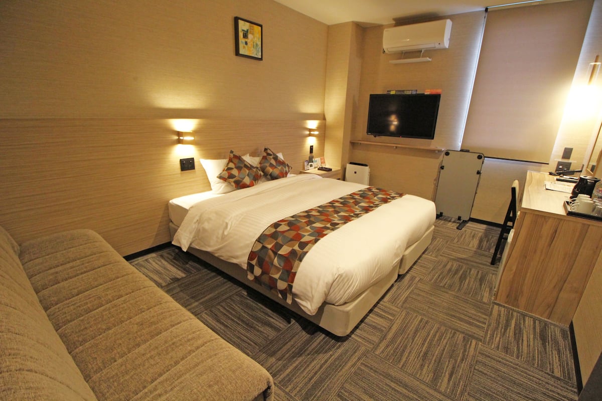 A hotel room with a large bed, a desk, a TV, and a small kitchenette.