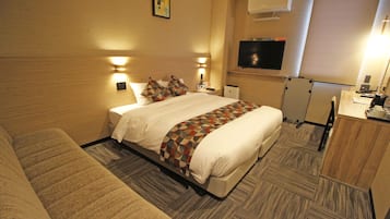 Quarto de hotel com uma cama grande, uma escrivaninha, uma televisão e uma kitchenette pequena.