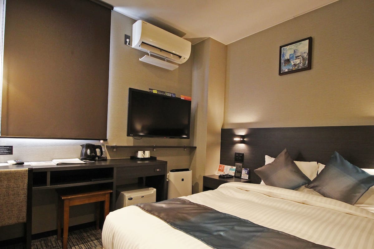 A hotel room with a bed, a desk, a chair, a television, and a coffee maker.