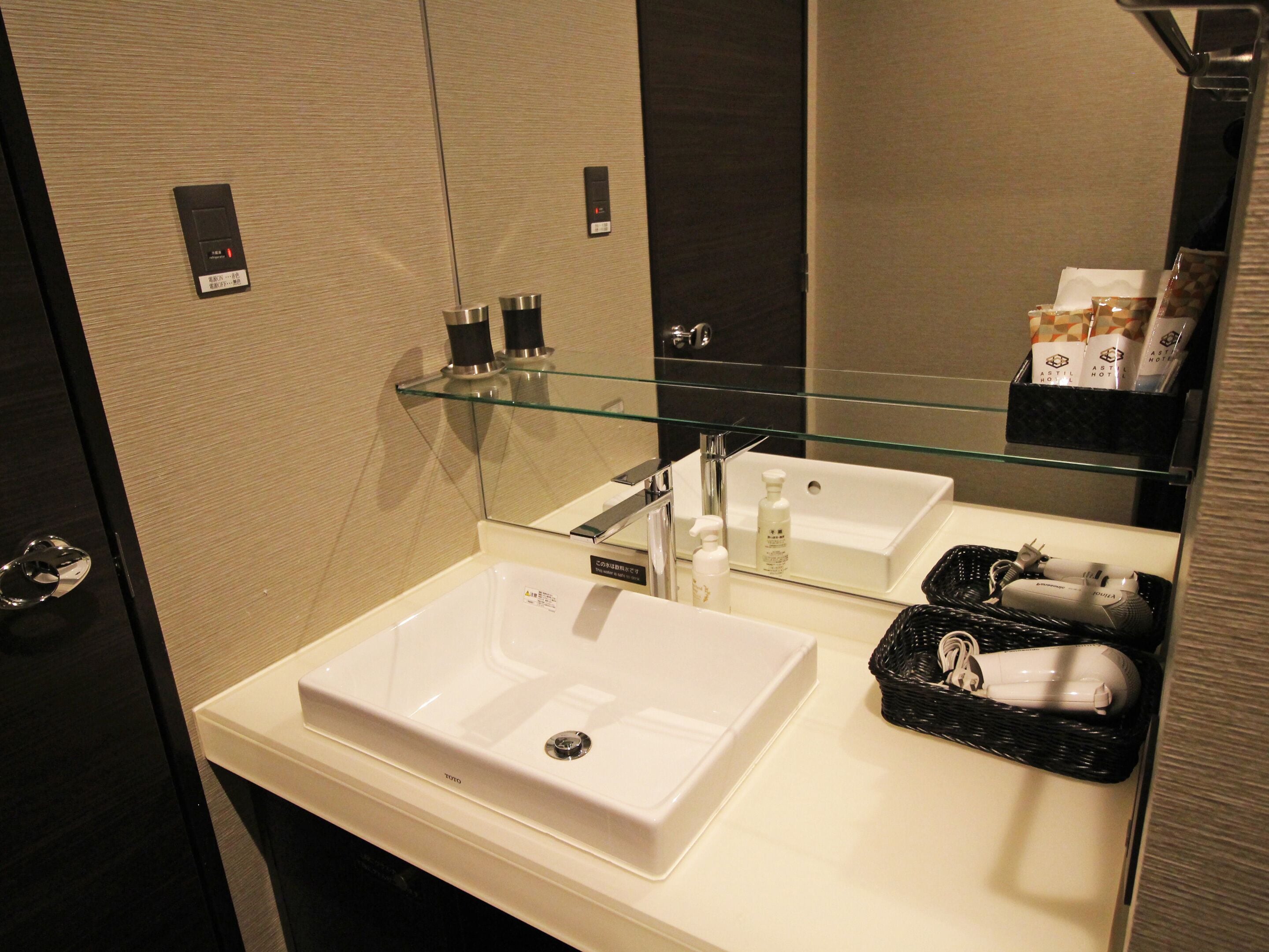 A modern bathroom with a white sink, a glass shelf above it, and a mirror reflecting the room.