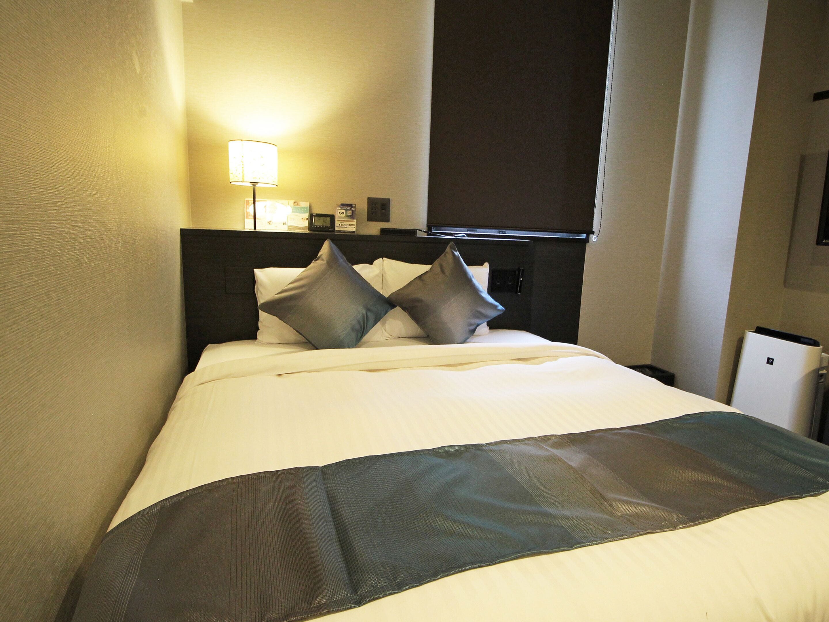 Una habitación de hotel con una cama, una mesita de noche, una lámpara y un televisor.