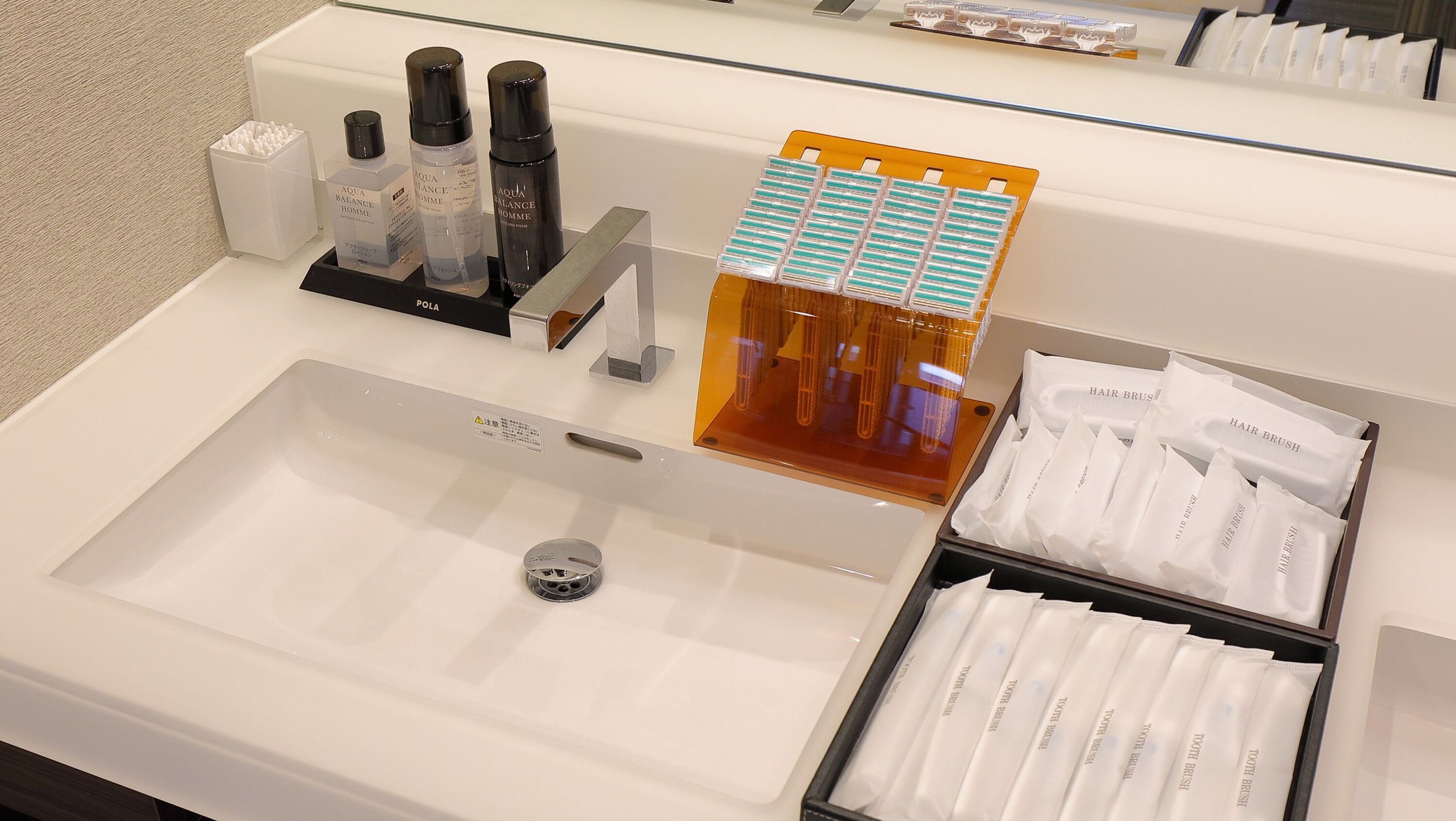 A hotel bathroom sink area with toiletries, including bottles and hairbrushes.