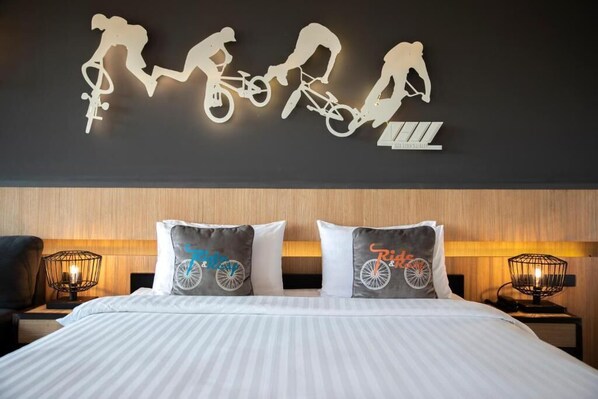 A hotel room with a bed, two nightstands, a wall-mounted light fixture, and a wall art piece depicting cyclists.