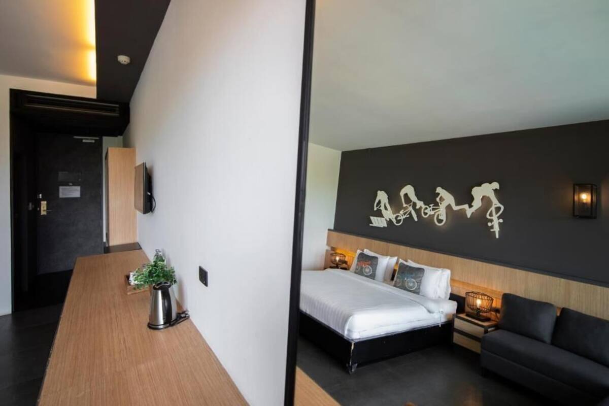 A modern hotel room with a bed, a sofa, a wooden desk, and a wall-mounted artwork.