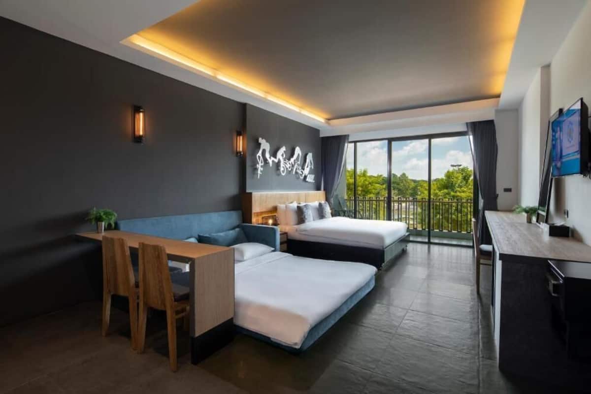 A modern hotel room with a sofa bed, a desk, and a balcony with a view.