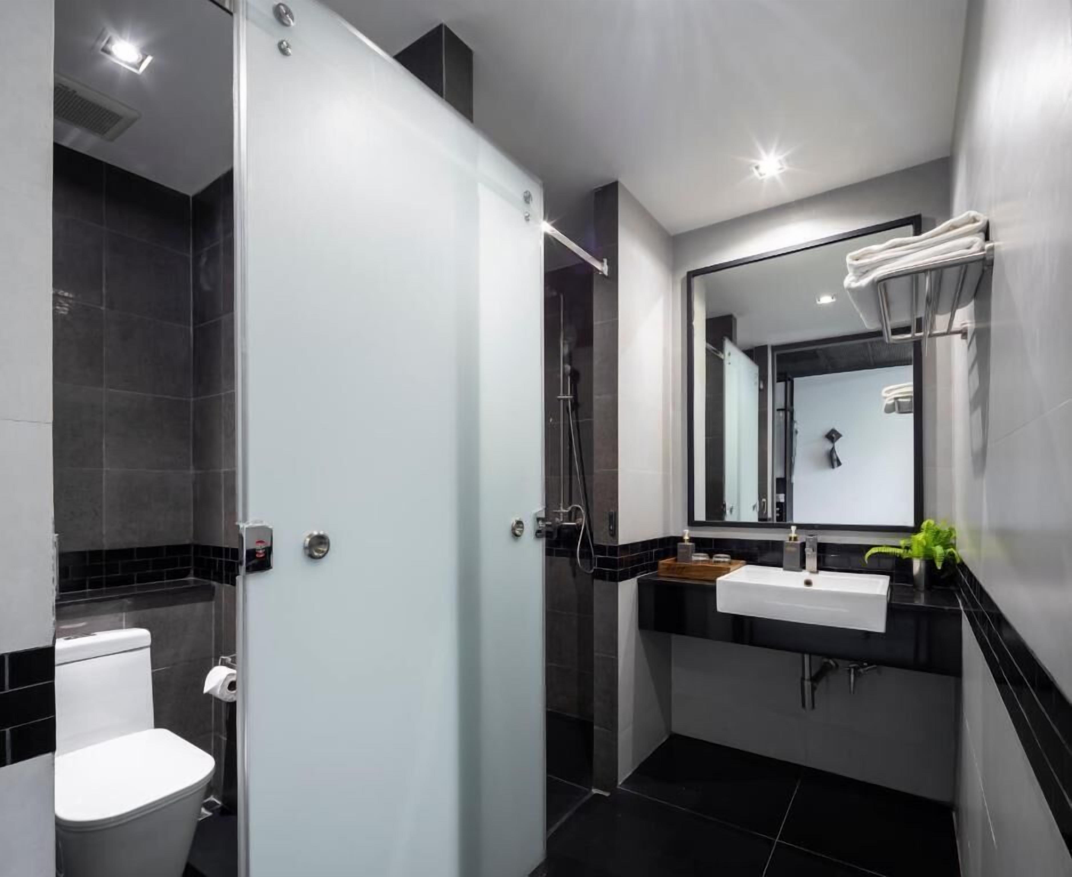 Un bagno moderno con box doccia in vetro, un water bianco, un mobile lavabo bicolore nero e bianco e uno specchio grande.