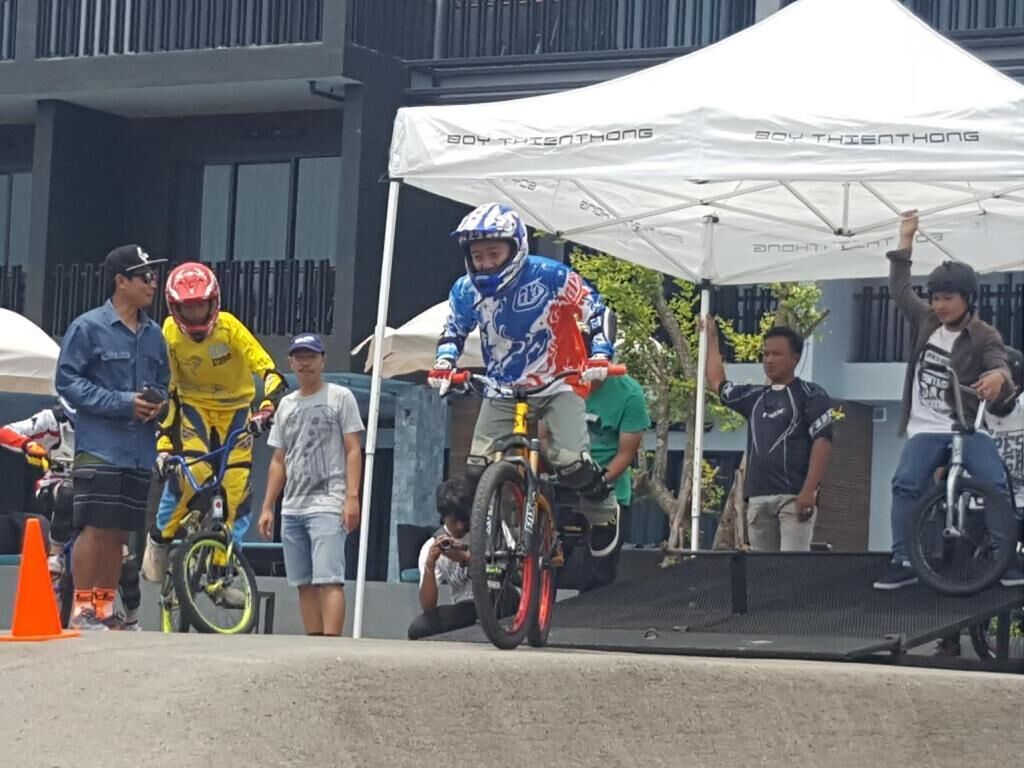 Un grupo de personas cerca de una zona de acrobacias con BMX, con una carpa con el letrero "SOY THIEN THONG" al fondo.