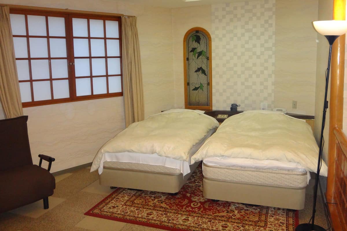 Una habitació d'hotel amb dos llits, un finestral gran amb cortines, un mirall decoratiu, una taula de nit i una làmpada de peu.
