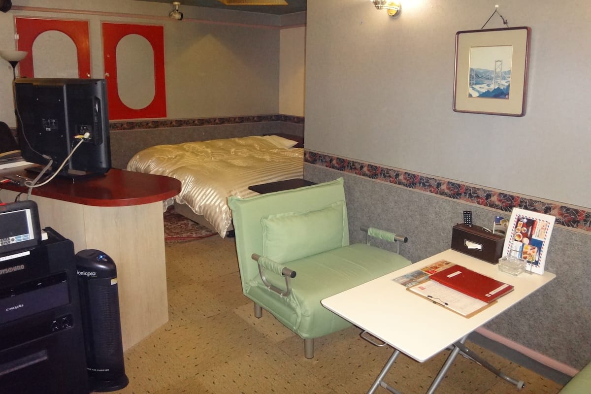 Habitació d'hotel amb un llit, escriptori amb ordinador, cadira, taula petita i un quadre amb marc a la paret.