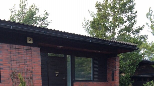 A modern brick house with a black door, stone steps, and a small garden with various plants. - Kotimaailma Apartments Naantali (Naantali)