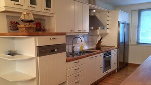 A modern kitchen with white cabinetry, a built-in dishwasher, a stainless steel range hood, and a refrigerator. - Kotimaailma Apartments Naantali (Naantali)