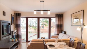 A modern living room with a sofa, dining table set for four, and a flat-screen TV mounted on the wall.