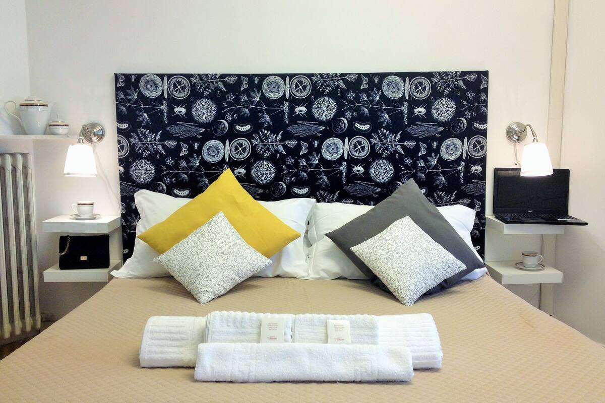 A neatly made bed with a patterned headboard, two bedside tables with lamps, and a laptop on one of the tables.