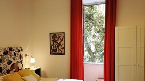 Una habitación de hotel con una cama, una mesita de noche, una lámpara, una ventana con cortinas rojas y una puerta.