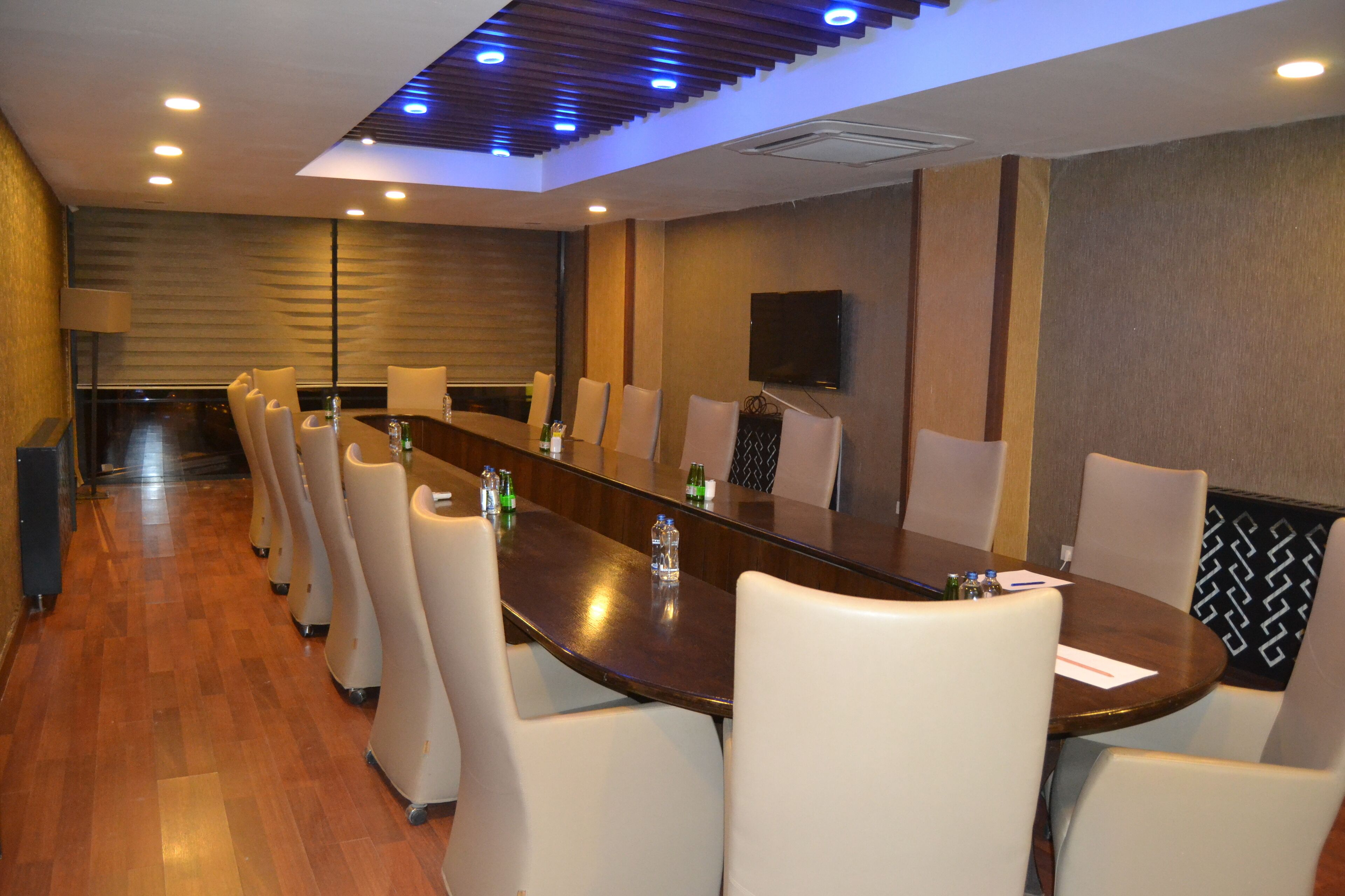 A conference room with a long table, white chairs, and a flat-screen TV mounted on the wall.