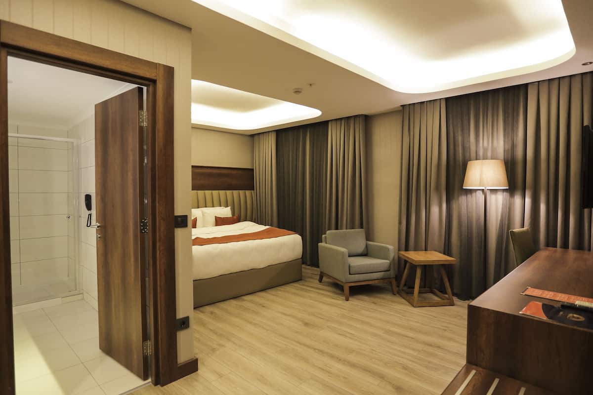 Une chambre d’hôtel avec un lit, une chaise, une petite table, une lampe et un téléviseur.