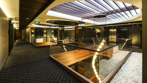 Un hall d’hôtel moderne avec une rambarde en verre, un comptoir d’accueil en bois et une verrière.