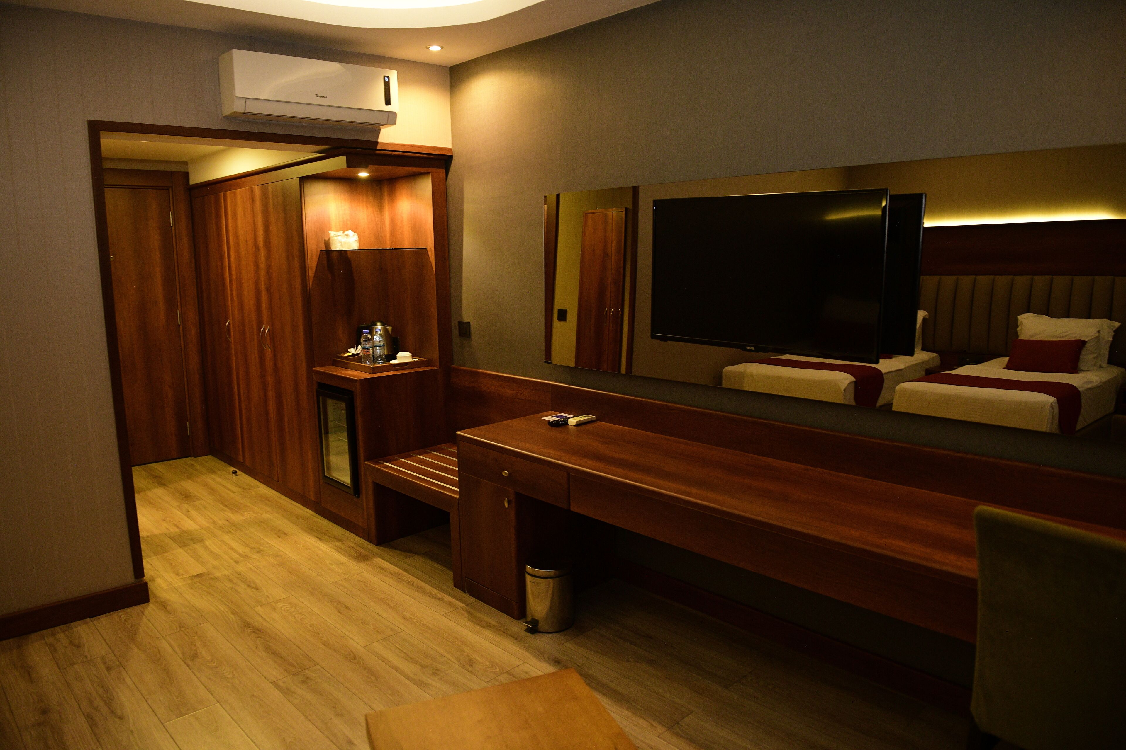 A hotel room with a wooden desk, a large mirror, a television, and a bed with pillows.