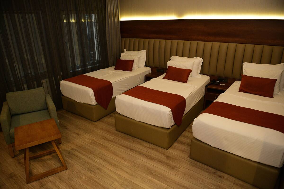 Une chambre d’hôtel avec trois lits, un petit coin salon et un plancher en bois.