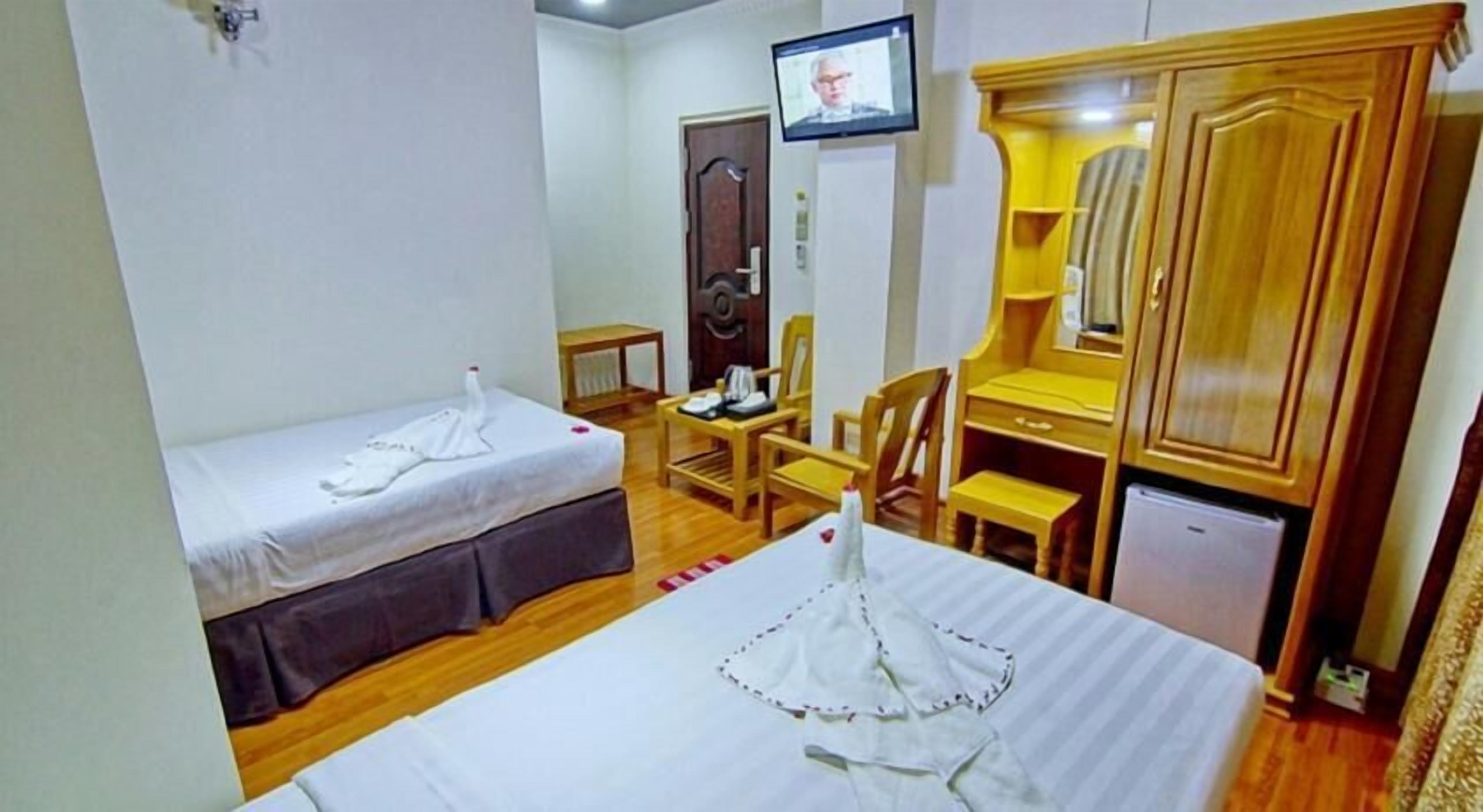 A hotel room with two single beds, a desk, a chair, a wardrobe, and a television.