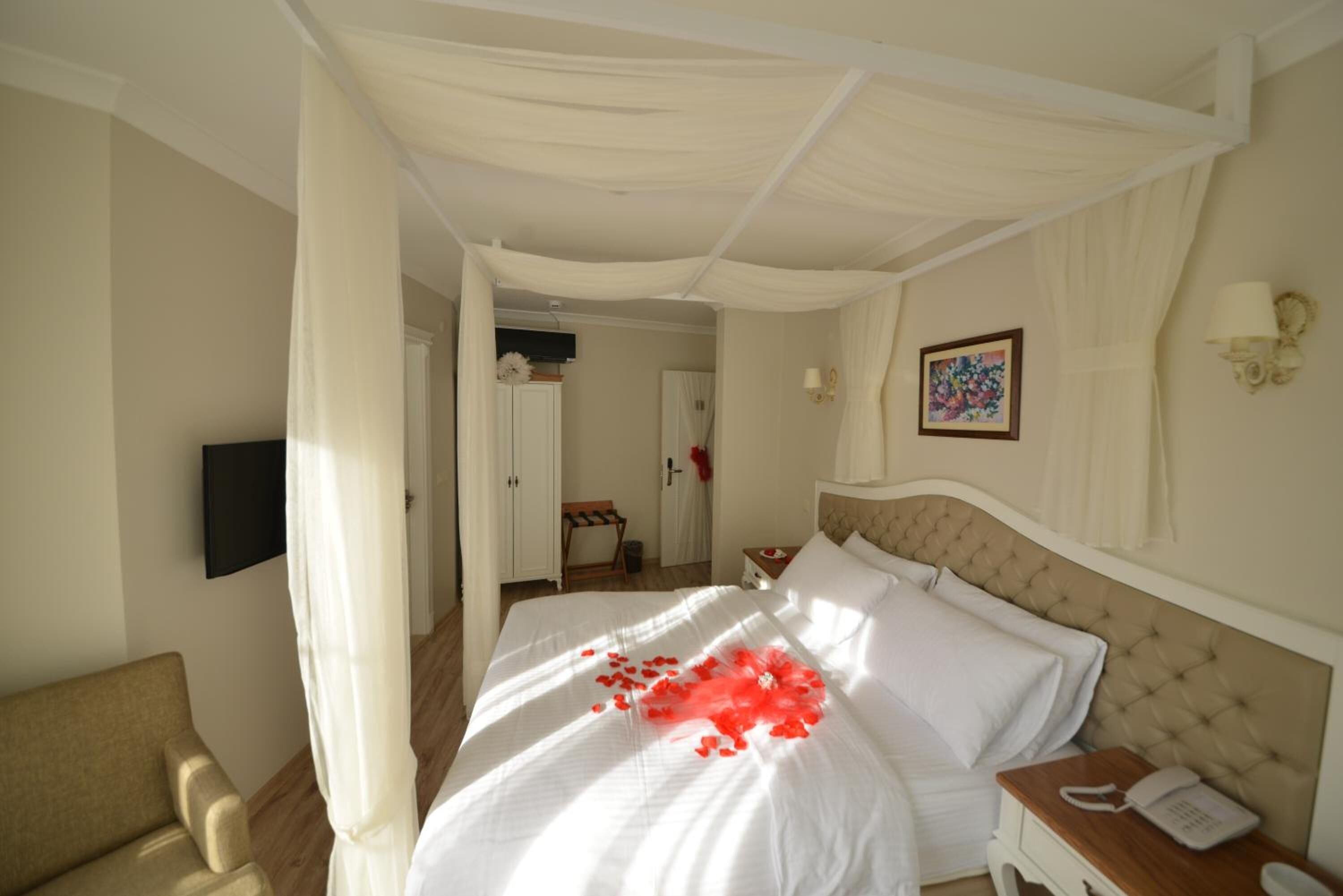 A hotel room with a bed, a bedside table with a phone, a chair, and a TV on the wall.