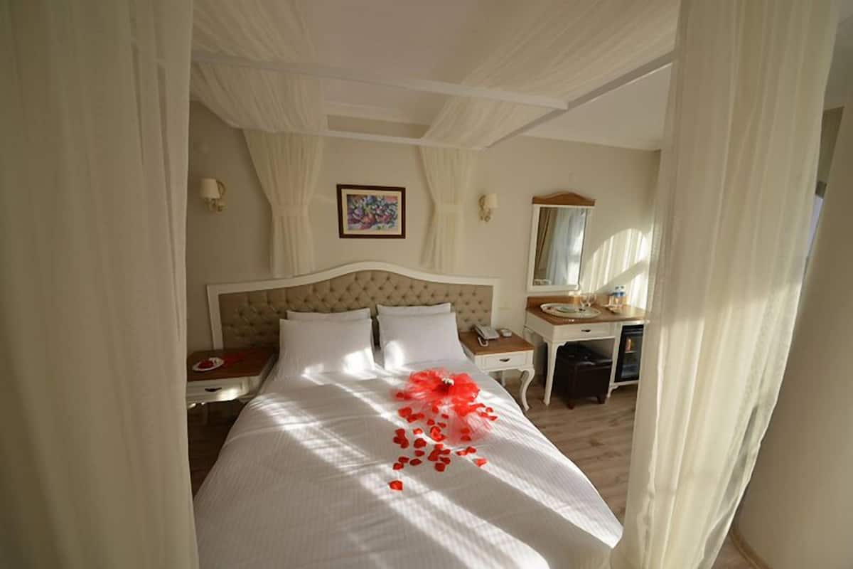A hotel room with a large bed, a bedside table, a desk, and a mirror.