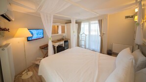 Habitación de hotel con una cama grande, un escritorio con computadora, televisor y ventana con cortinas.