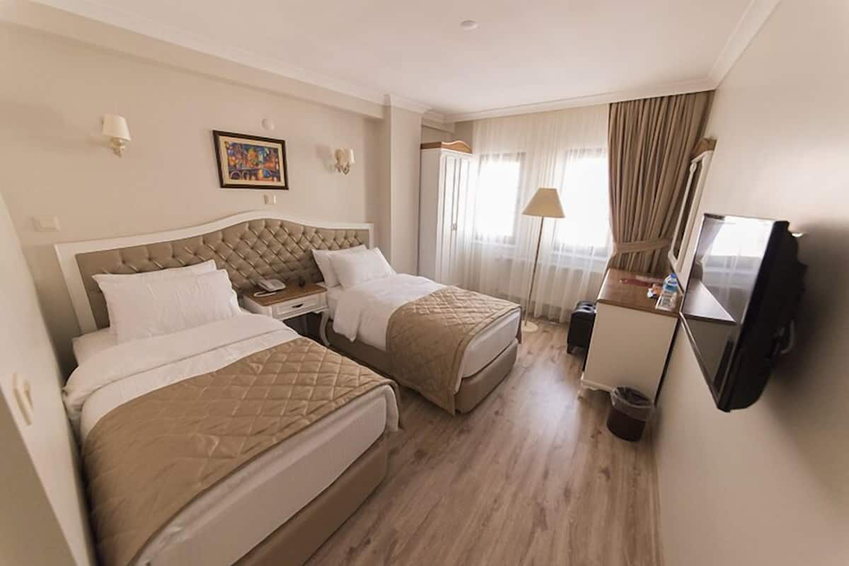 A hotel room with two beds, a desk, a television, and a window with curtains.