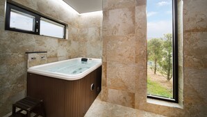 A modern bathroom with a hot tub, a window with a view of trees, and a wooden stool.