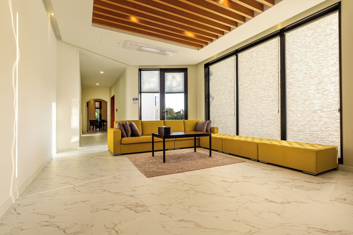A modern living room with a yellow sofa, a coffee table, and a large window with blinds.