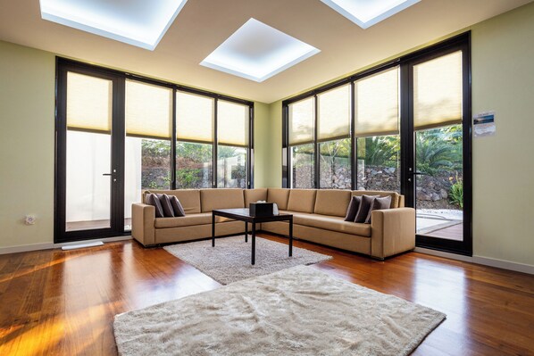 A spacious living room with a sectional sofa, a coffee table, and a large window with a view of greenery.