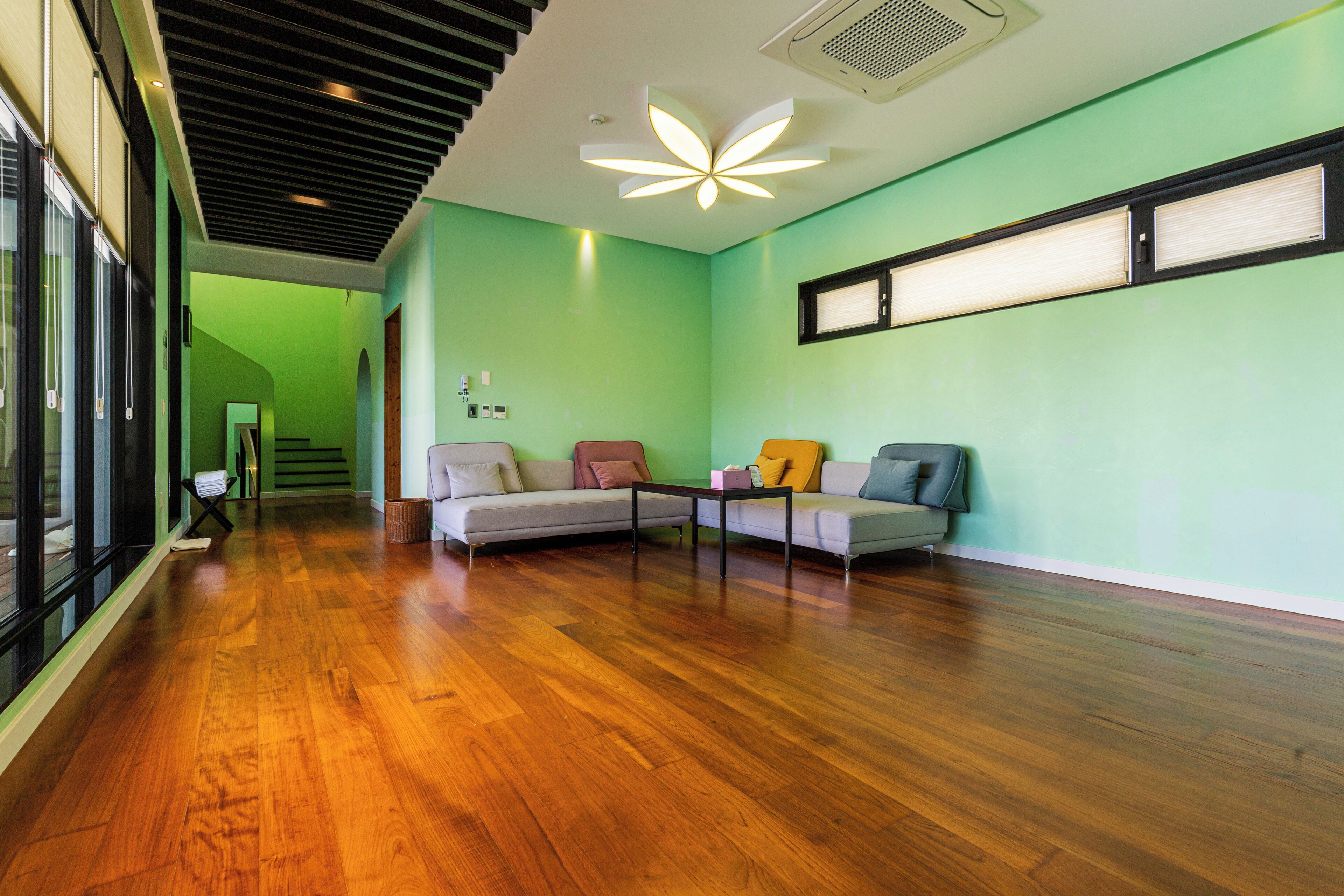 A spacious room with a wooden floor, a sectional sofa, and a modern ceiling light fixture.
