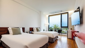 A hotel room with two beds, a desk, a chair, a TV, and a window with a view of palm trees.