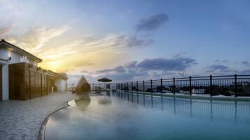 A pool area with a building, a fence, and a sunset.