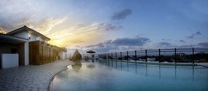 A pool area with a building, a fence, and a sunset. - Libentia Hotel & Pool Villa (Jeju City)