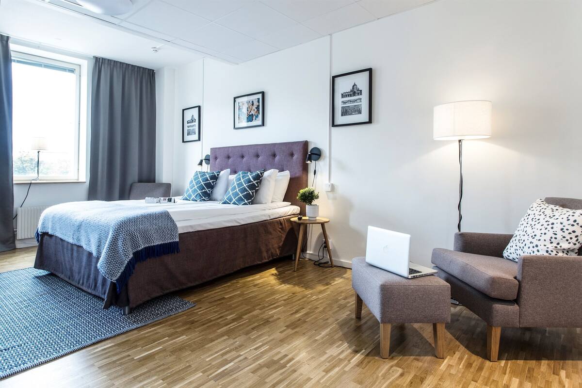 Een moderne hotelkamer met een groot bed, een bureau met een laptop, een bank en een staande lamp.