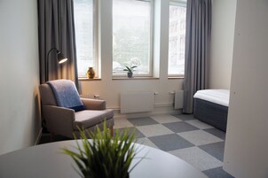 Quarto moderno e compacto com sofá, uma mesinha, uma planta em vaso e uma cama.