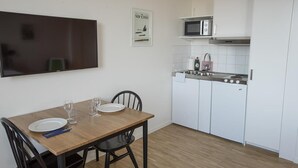 Une cuisine compacte avec des meubles blancs, un four à micro-ondes et un évier. On y trouve une table à manger avec des chaises et un téléviseur fixé au mur.