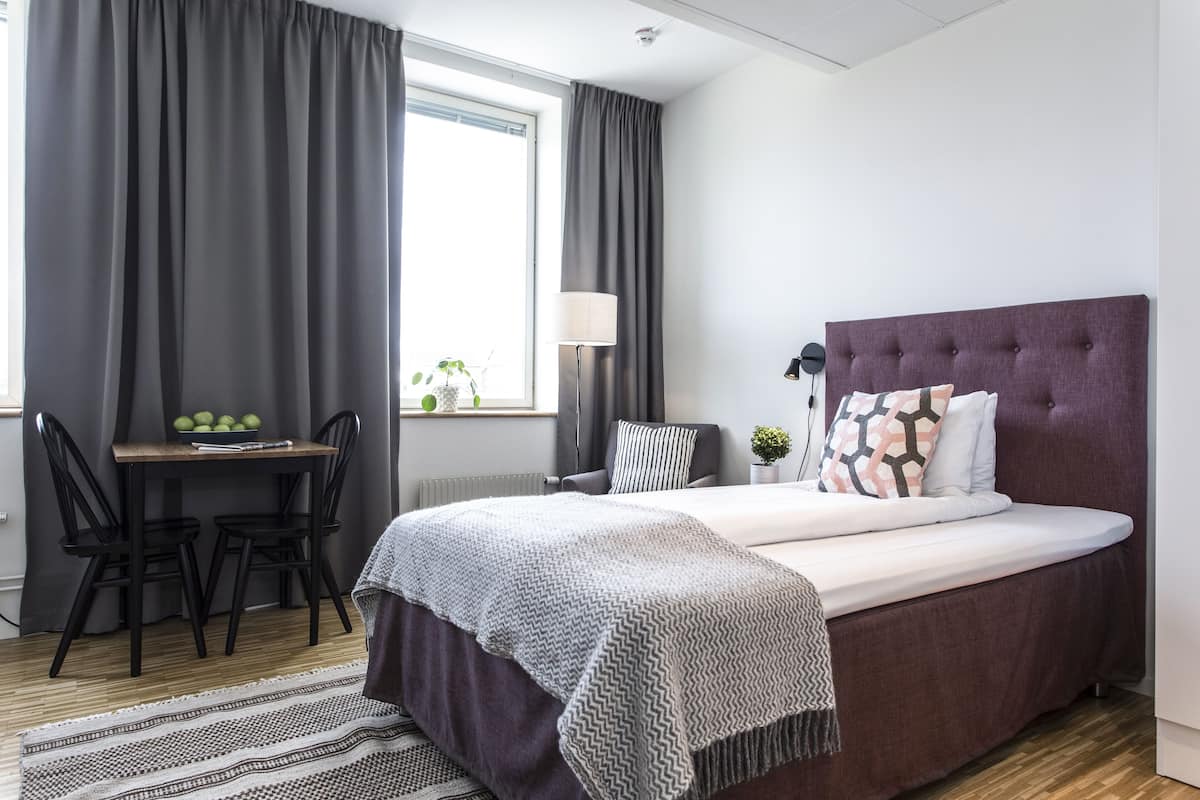 Een slaapkamer met een bed, een bureau, stoelen, een lamp en een raam met gordijnen.