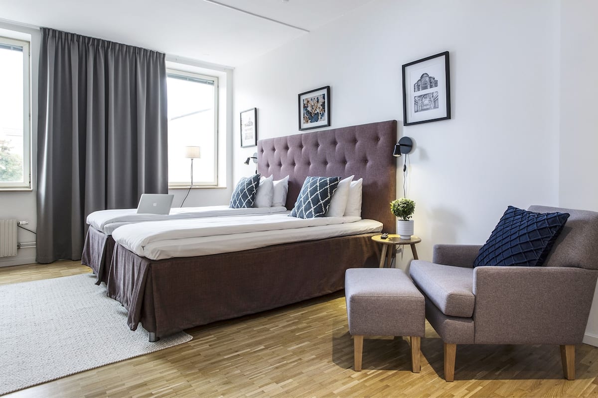 Een moderne slaapkamer met een groot bed, een bureau, een stoel en een bijzettafeltje met een plant.