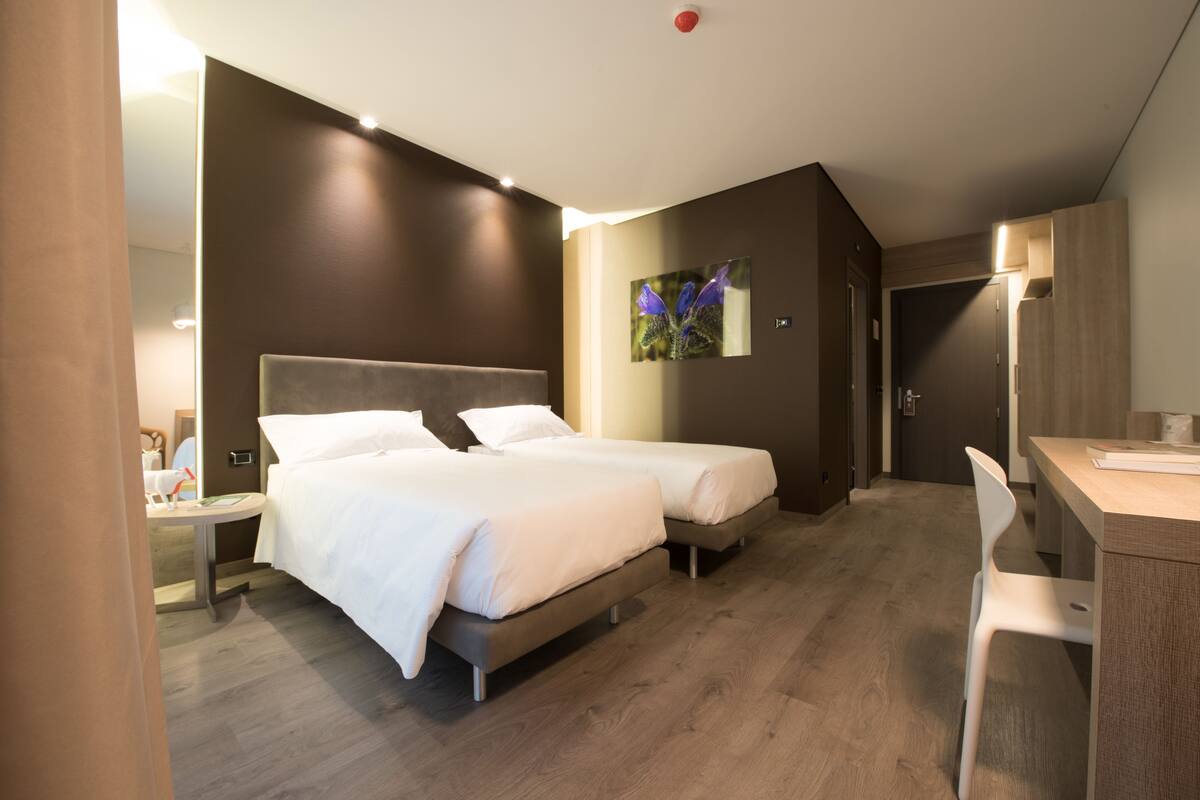 A modern hotel room with two beds, a desk, and a chair.
