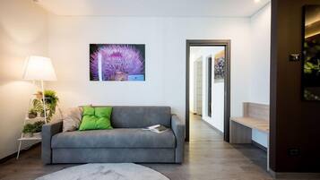Een moderne woonkamer met een grijze bank, een ronde salontafel en een schilderij van paarse bloemen aan de muur.