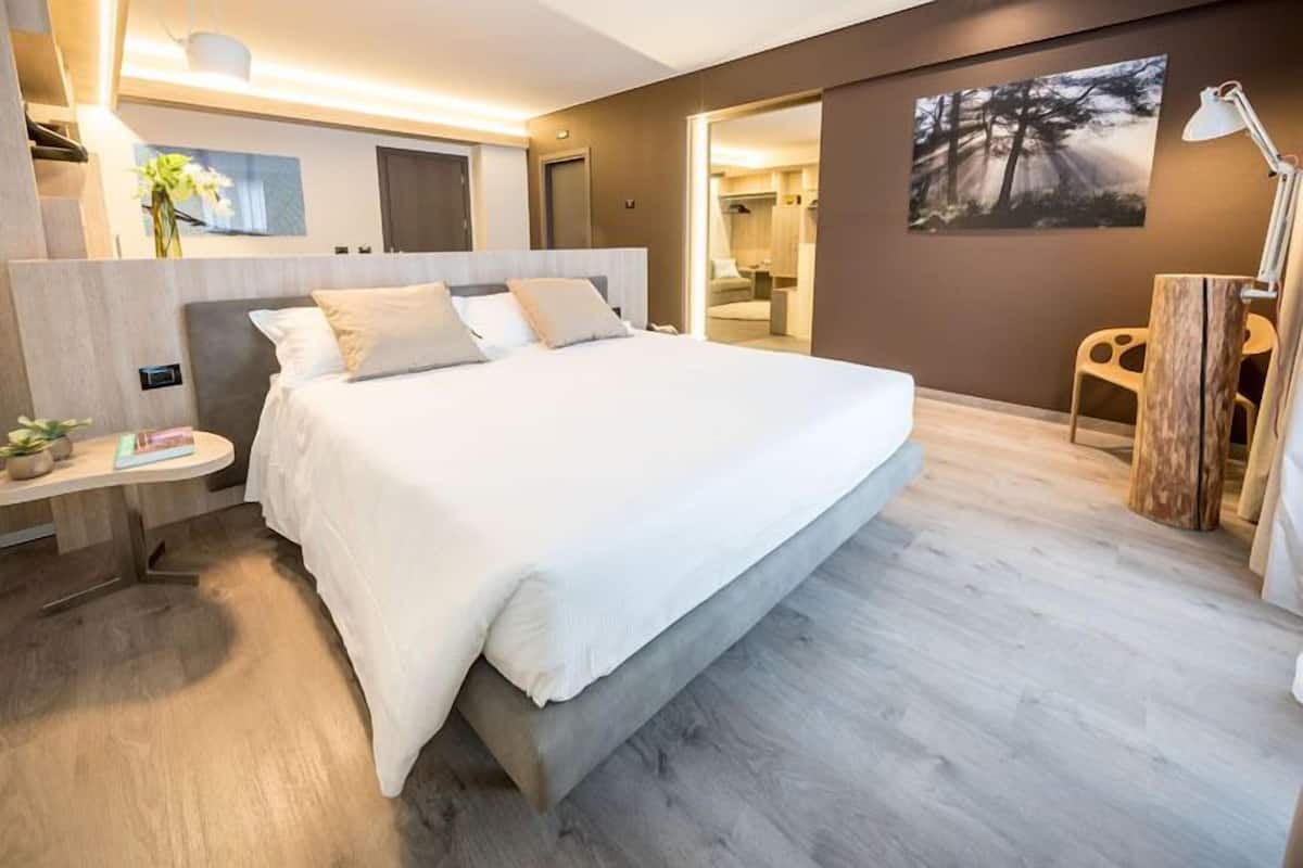 A modern hotel room with a large bed, a bedside table with a lamp, and a view of the bathroom through an open door.