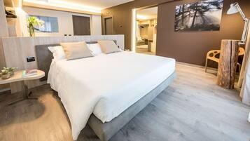Una habitación de hotel moderna con una cama grande, una mesita de noche con lámpara y vistas al baño a través de una puerta abierta.