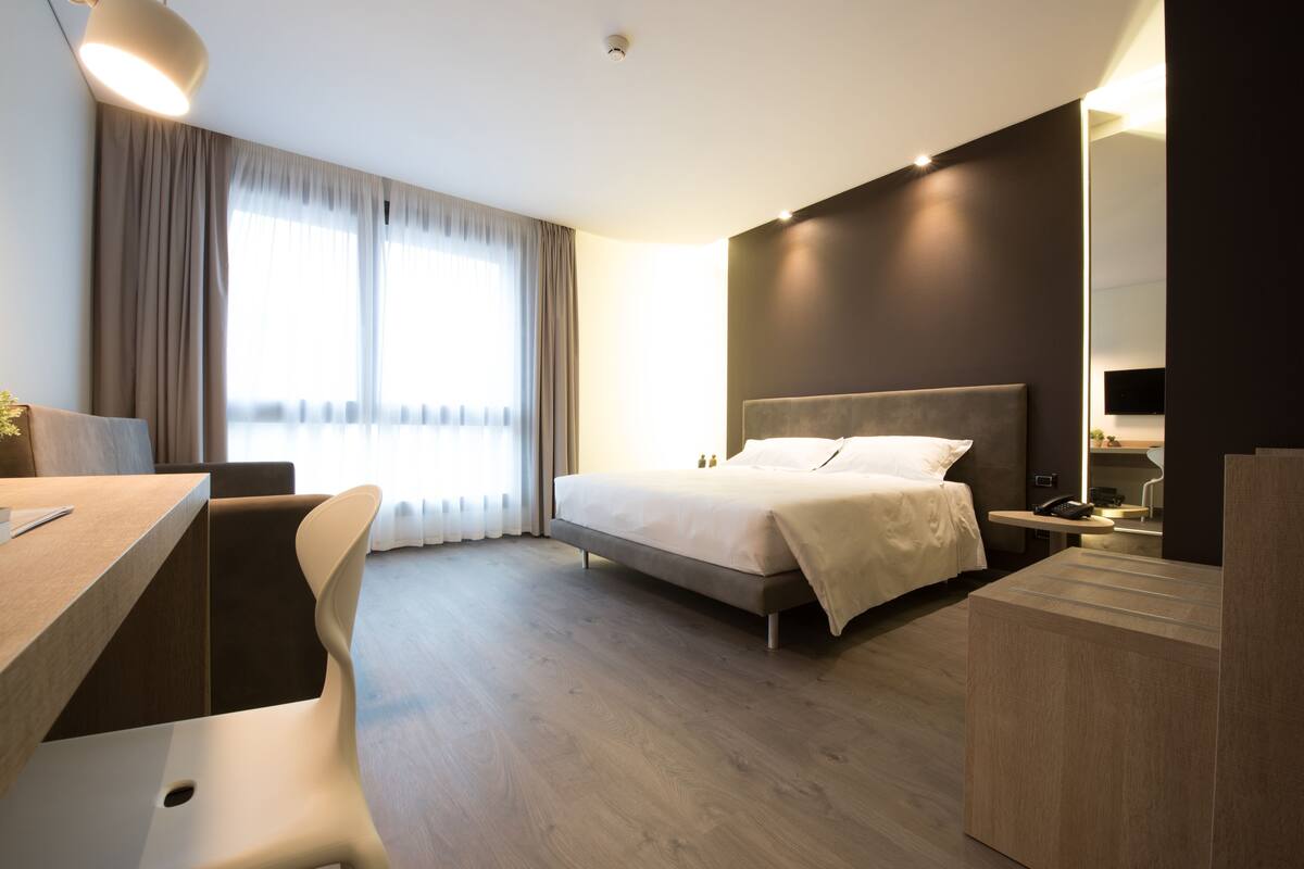 A modern hotel room with a large bed, a desk, and a chair.